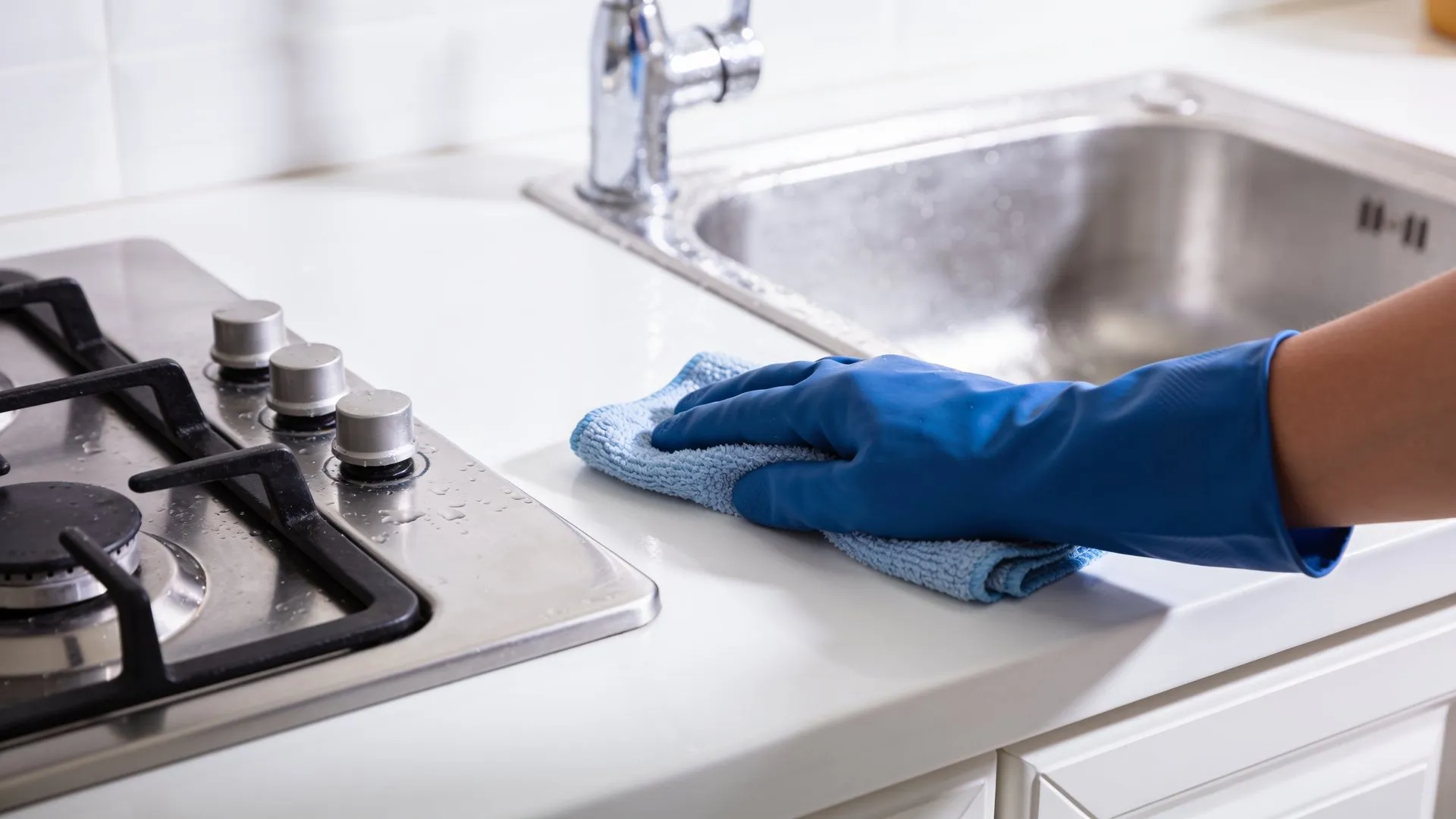 Hand in a blue glove wiping a kitchen counter